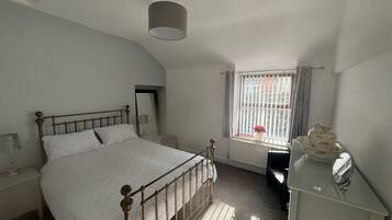 A bedroom with a bed, a nightstand, a dresser, a mirror, a window with curtains, and a radiator.