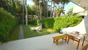 A patio area with a tiled floor, a wooden table, and white chairs. - Holiday Villa With Garden (Lignano Sabbiadoro)