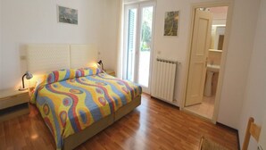 Une chambre à coucher comprenant un lit, des lampes de chevet, un radiateur, une porte donnant sur une salle de bain et une chaise.