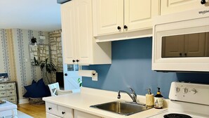 Una cocina con armarios blancos, microondas, estufa y pileta.