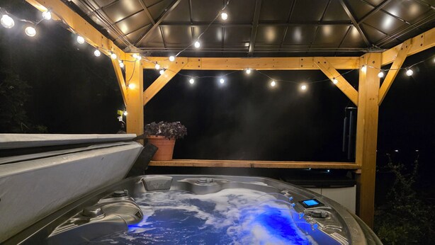 Ein Whirlpool unter einer Hollaube mit Lichterketten, umgeben von dunklem Nachthimmel.