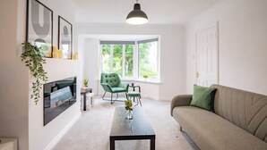 Ein modernes Wohnzimmer mit einer Couch, einem Couchtisch, einem Fernseher und einem Fenster mit Blick auf Grünflächen.