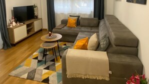 A modern living room with a sofa, a small round table, a flat-screen TV, and a decorative plant.