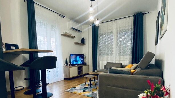 A modern living room with a sofa, a dining area with chairs, a TV, and a ceiling fan.