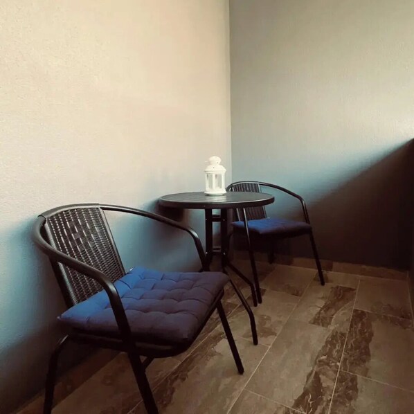 Eine Sitzecke mit zwei schwarzen Metallstühlen, blauen Kissen und einem kleinen runden Tisch mit einer weißen Laterne.