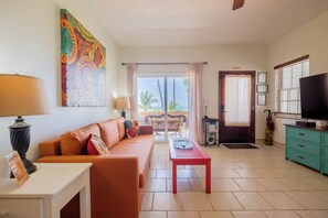 A living room with a sofa, a coffee table, a TV, a painting, and a balcony with a view.