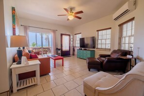 Una sala de estar con sofá, sillón, televisor, ventilador de techo y vistas al exterior.