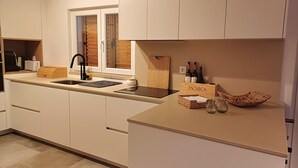 Een moderne keuken met witte kasten, een houten aanrecht, een inbouwspoelbak en een raam met houten jaloezieën.