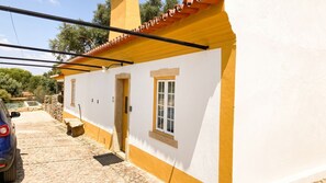 Un bâtiment blanc avec un toit jaune, un mur en pierre et une voiture garée devant.