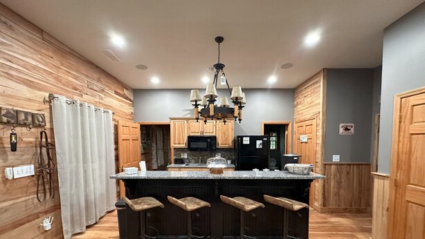 Eine Küche mit Holzausstattung, einer zentralen Kochinsel mit Barhocker, einer Chandelierleuchtre und einem Kühlschrank.
