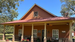 Ein Haus mit überdachter Veranda, Steinsäulen und Sitzgelegenheiten im Freien.