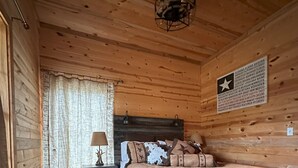 Ein Schlafzimmer einer Holzhütte mit Bett, Nachttisch, Lampe und einer Wand mit einem Sternemblem.