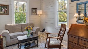 A cozy living room with a striped sofa, a wooden rocking chair, a coffee table with a vase of flowers, and a wooden dresser.