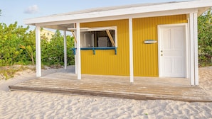 Et strandhus med en overdækket veranda, en dør og et lille udendørs siddeområde.