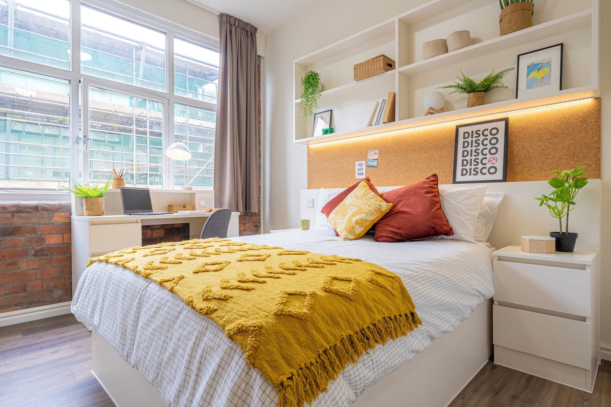 A modern bedroom with a large bed, a desk, and a window with a view of a building.