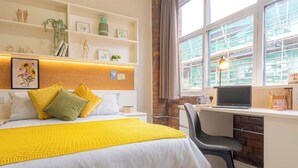 Hotelkamer met een bed, een bureau met een laptop, een stoel en een raam met uitzicht op de bouw buiten.