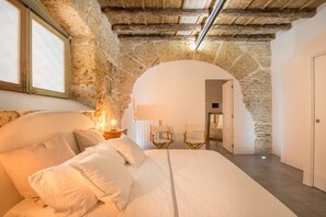 A bedroom with a stone archway, a bed with white linens, and a nightstand with a lamp. - Stylish Home in Front of Casa Professa by Wonderful Italy (Palermo)
