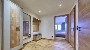 Ein Zimmer mit Holzboden, einem großen Spiegel, einer hölzernen Bank und einer Tür zu einem weiteren Raum.