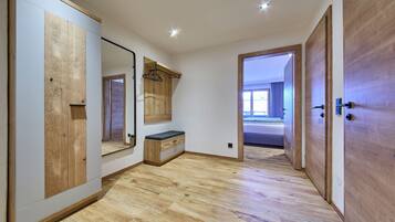 Ein Zimmer mit Holzboden, einem großen Spiegel, einer hölzernen Bank und einer Tür zu einem weiteren Raum.