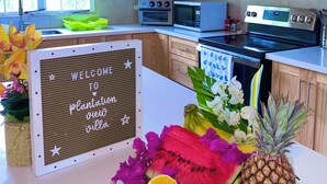 Een keuken met houten kastjes, een fornuis, een magnetron en een spoelbak. Op het aanrecht staat een bord met fruit en een welkomstbord.