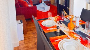 Un coin repas avec une nappe rouge et orange, des assiettes blanches et un vase décoré de branches.