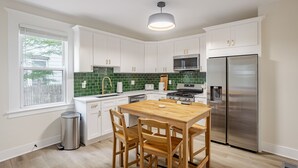 Een moderne keuken met witte kasten, een groene achterwand, roestvrijstalen apparatuur en een houten eettafel.