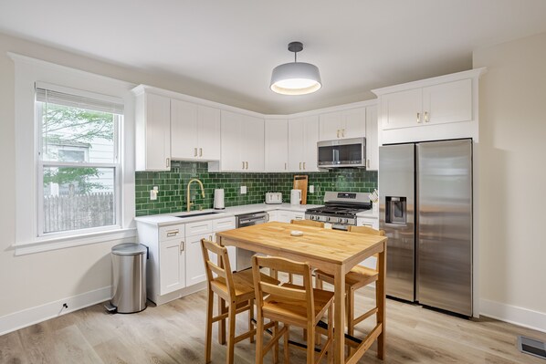 A modern kitchen with white cabinets, a green backsplash, stainless steel appliances, and a wooden dining table.
