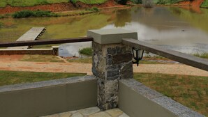A stone bridge over a calm river, surrounded by green hills and mountains under a partly cloudy sky. - Fazenda Capuava (Bananal)