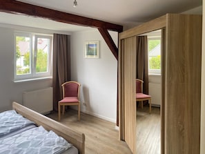 Une chambre à coucher avec un lit, deux chaises, une fenêtre et un miroir.