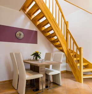 A dining area with a wooden staircase, a clock on the wall, and a table with chairs.