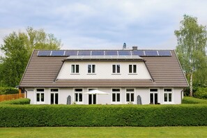 Une maison à deux étages, dotée de panneaux solaires sur le toit, d’une haie bien entretenue et surplombant un ciel dégagé.
