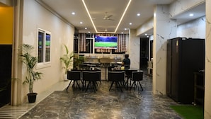 A modern kitchen with a TV, dining area with chairs, and a refrigerator. - GVP Residency (Bengaluru)
