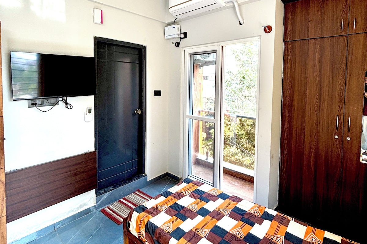 A bedroom with a bed, a ceiling fan, an air conditioning unit, a TV mounted on the wall, and a wardrobe.