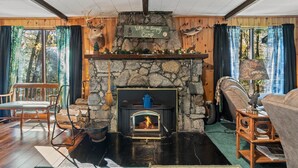 A cozy cabin interior with a stone fireplace, wooden furniture, and a sign that reads "Life is Simply Camp."