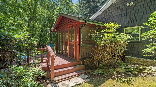 A wooden deck with a red railing, surrounded by lush greenery and a stone pathway.