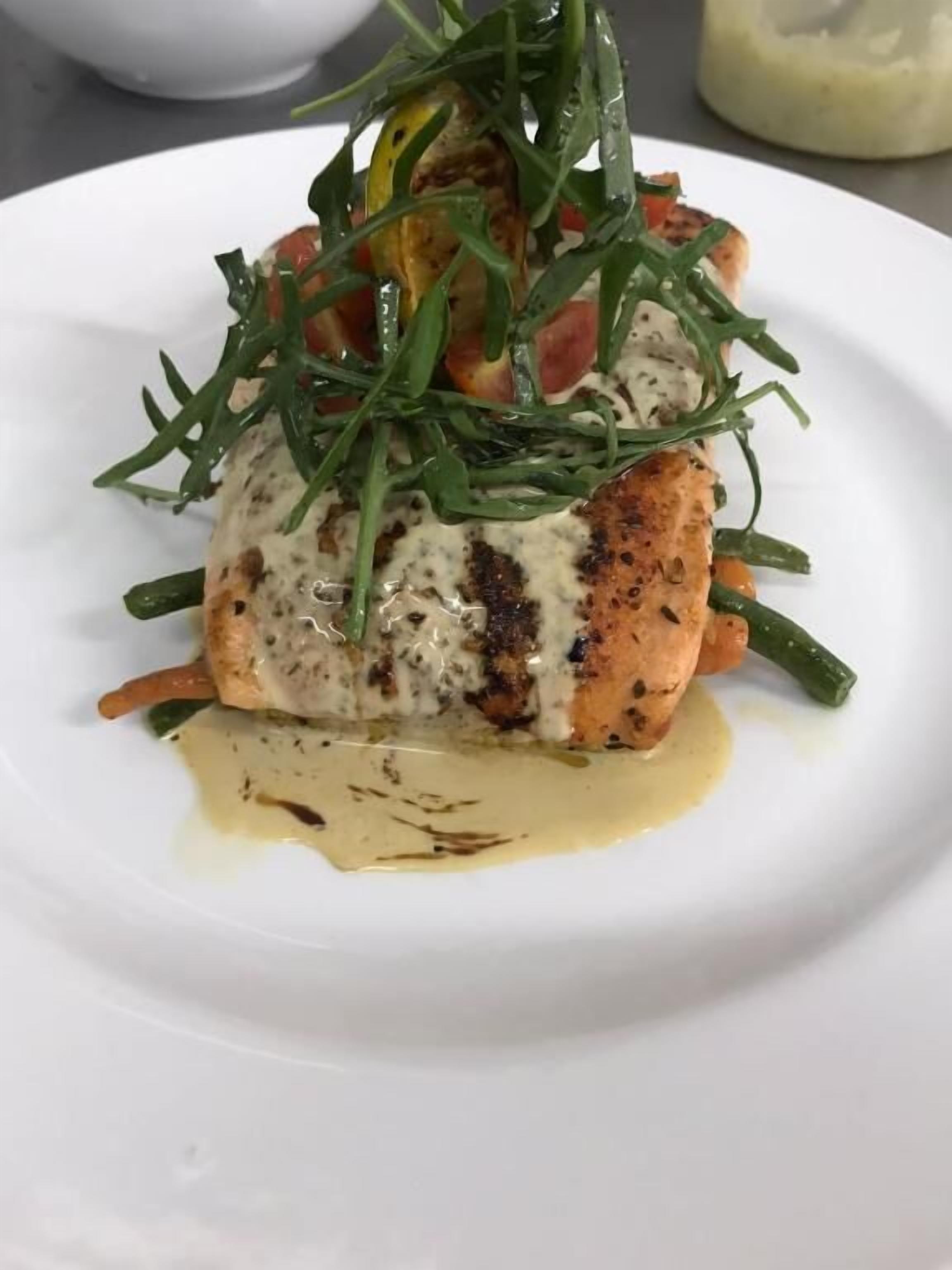 A plate with a piece of grilled fish topped with greens and a creamy sauce.