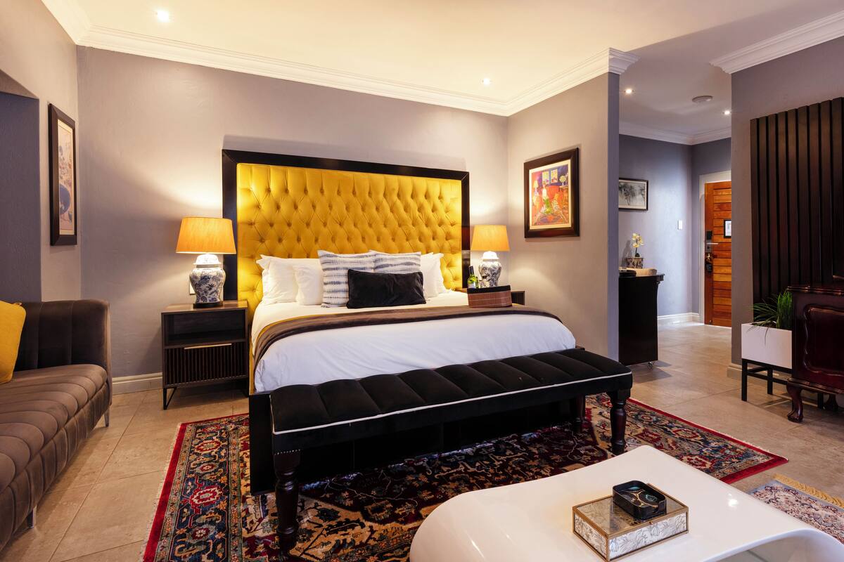 A modern hotel room with a large bed, two bedside tables, a bench, a sofa, and a coffee table.