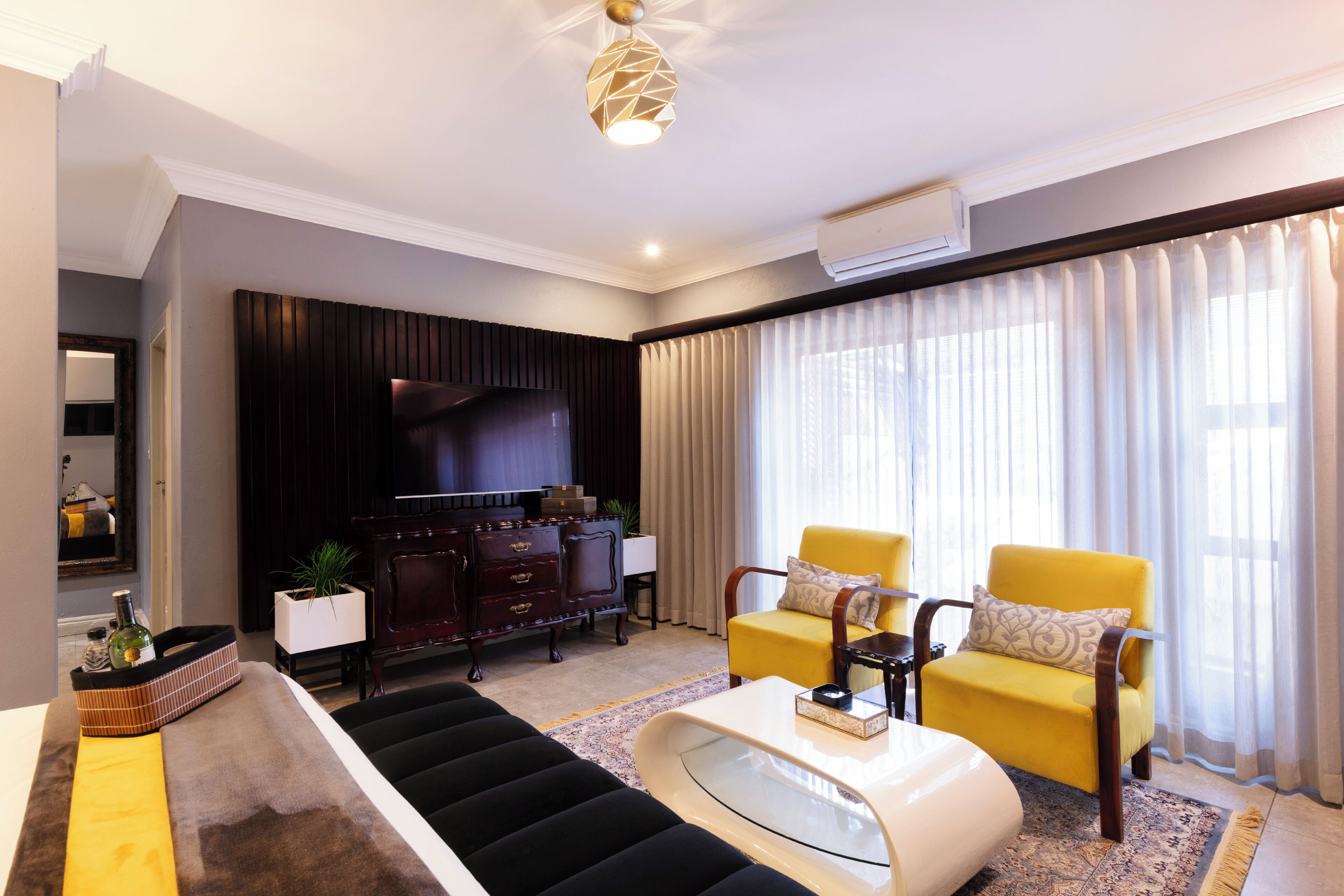 Un salon moderne comprenant un canapé, deux fauteuils jaunes, une table basse, un téléviseur à écran plat et une plante décorative.