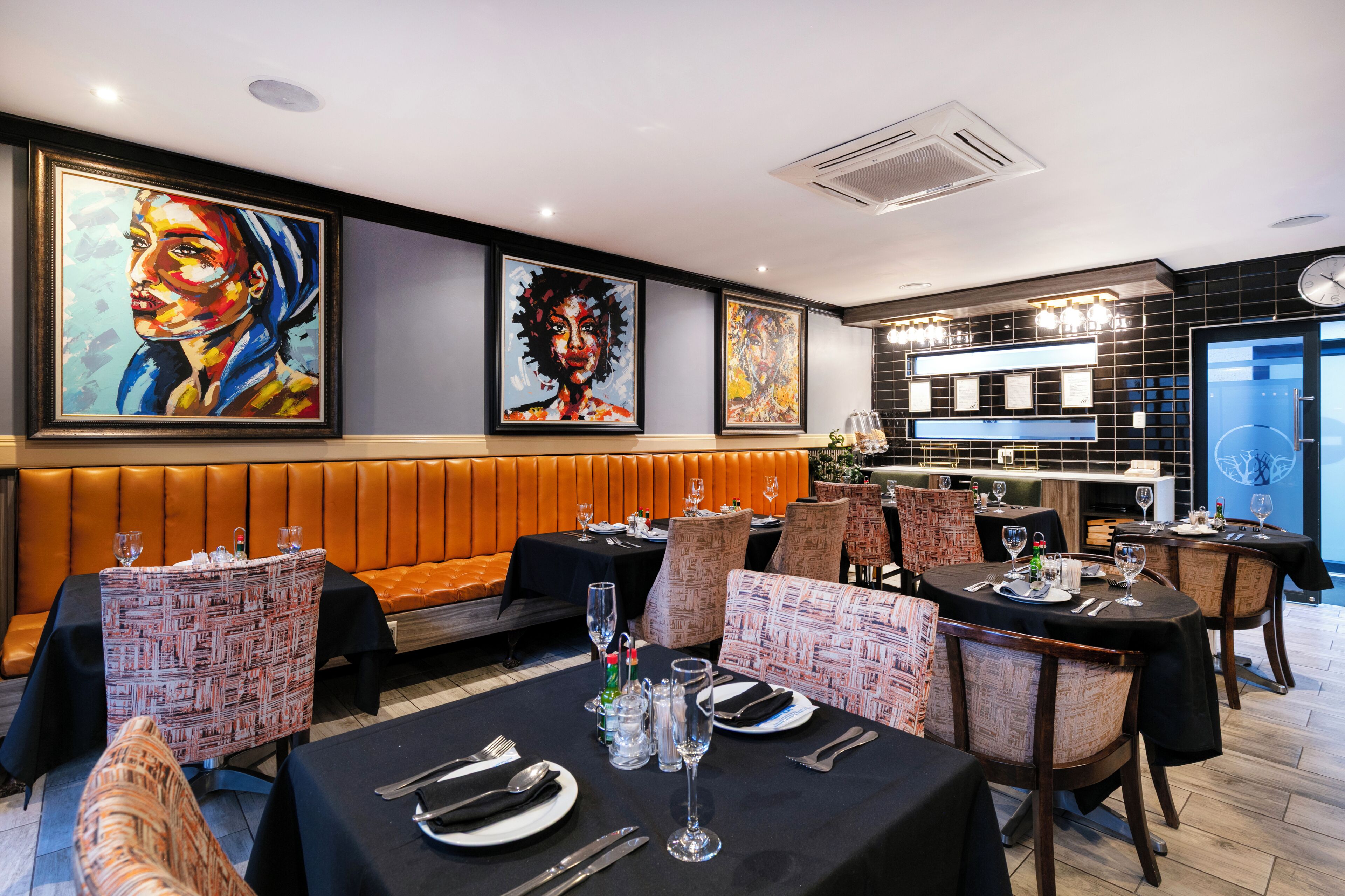 Un restaurant avec des tables dressées pour le service, un bar et des œuvres d’art accrochées aux murs.