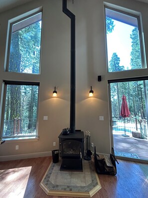Huone, jossa on takka, suuret ikkunat ja näkymä metsään.