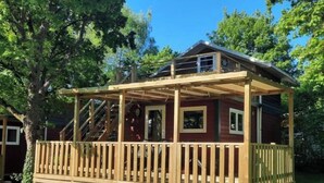 Eine Holzterrasse mit Treppe zu einem überdachten Bereich, umgeben von Bäumen.