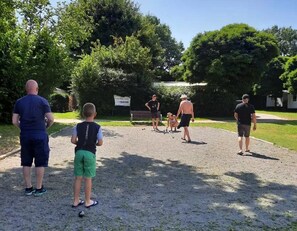 A group of people playing croquet in a park with trees and a sign in the background.