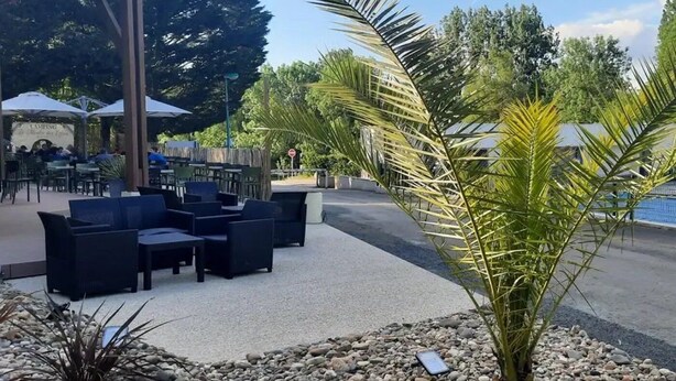Un espace extérieur aménagé avec des tables et des chaises, entouré d’un chemin de gravier et de plantes tropicales.