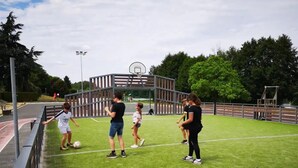 Un complexe sportif extérieur comprenant un terrain de basket-ball, une zone délimitée par une clôture et un terrain enherbé.