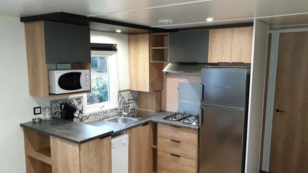 Een compacte keuken met houten kastjes, een magnetron, een gasfornuis en een inbouwvaatwasser.