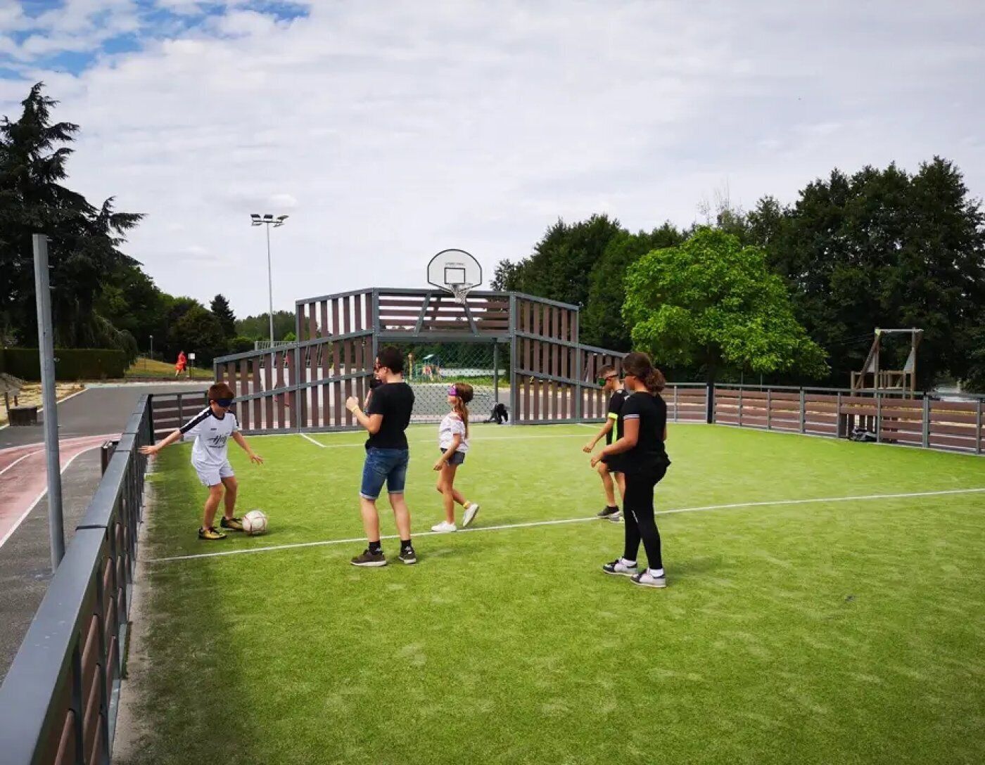 Eine Sportanlage im Freien mit Basketballfeld, einem eingezäunten Bereich und einer Rasenfläche.