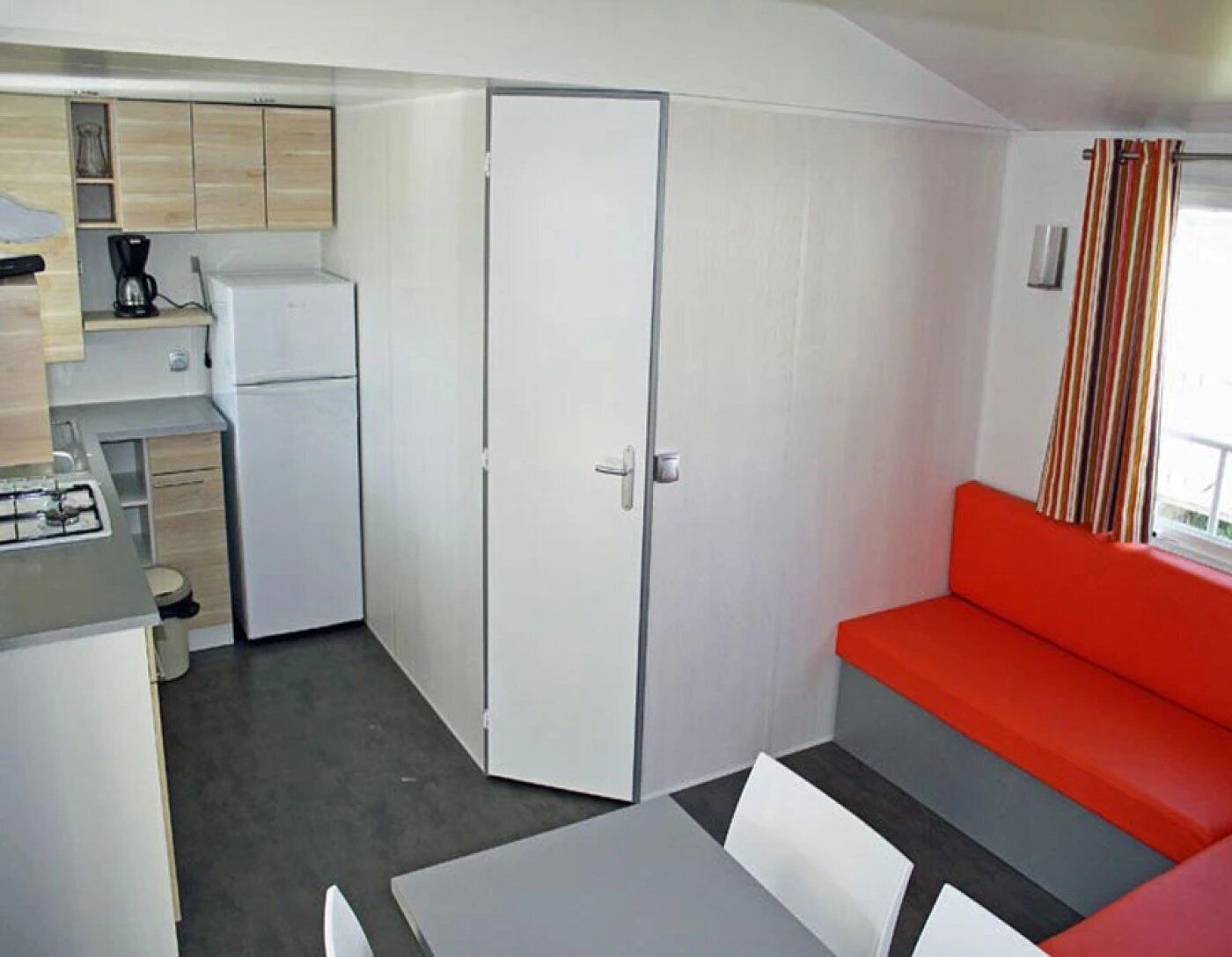 A compact room with a kitchenette, a dining area, and a red sofa.