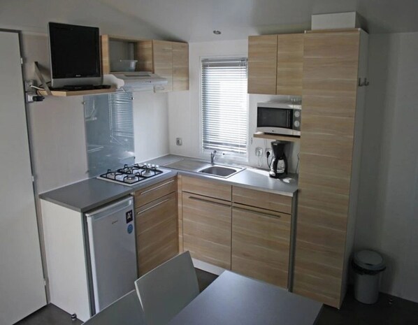 Una cocina compacta con estufa a gas, lavamanos, microondas y un refrigerador pequeño.