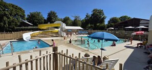 Un espace piscine comprenant un toboggan aquatique, plusieurs piscines et des parasols pour se protéger du soleil.