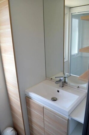 Een badkamer met een wit wastafel, een spiegel en een houten kastje.